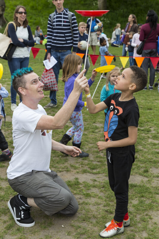 Paul from Kinetic Circus helping a child learn to do a spinning plate at a circus workshop